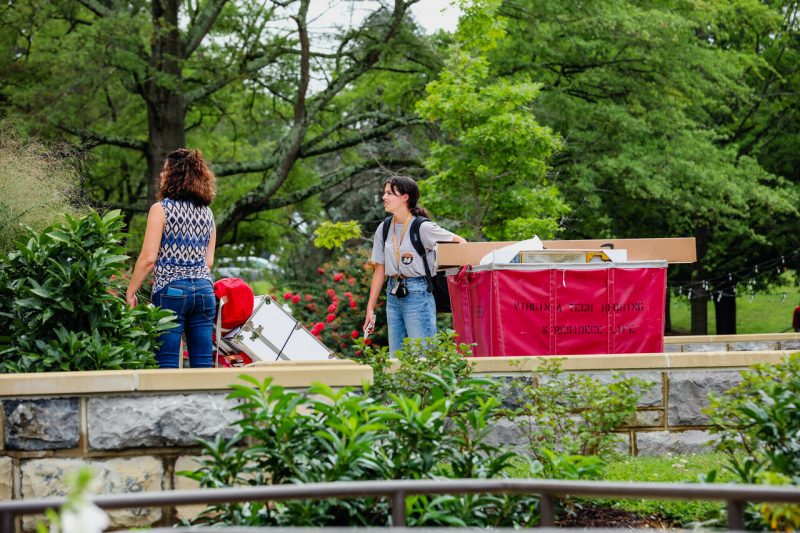 Two people pull large carts full of dorm materials on a sunny day